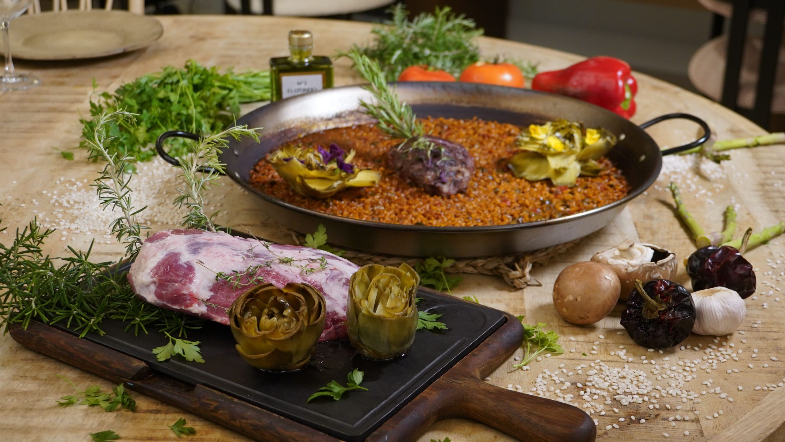 Una paella valenciana tradicional, bellamente presentada con alcachofas, carne y verduras frescas sobre una mesa rústica.